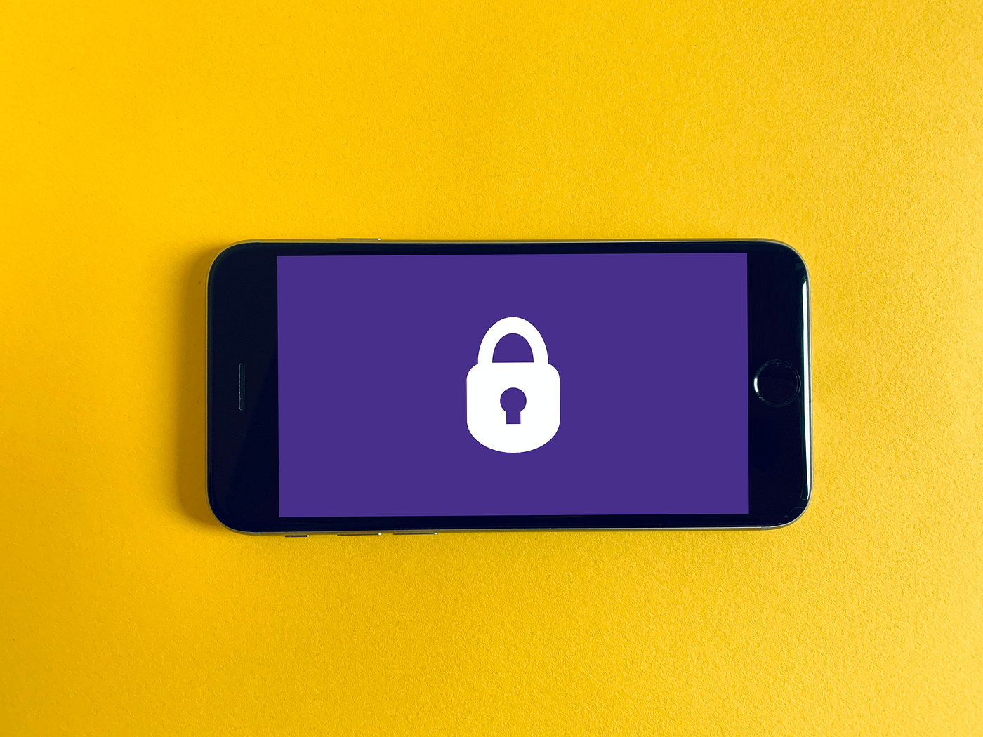 A smartphone displaying a lock icon on a purple screen, resting on a yellow background